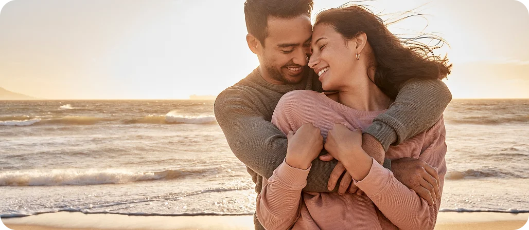 Romantic couple embracing on beach at sunset with ocean waves in background - In Los Angeles, CA