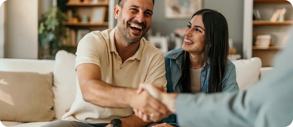 Happy couple shaking hands with advisor during home consultation meeting on couch - In Los Angeles, CA