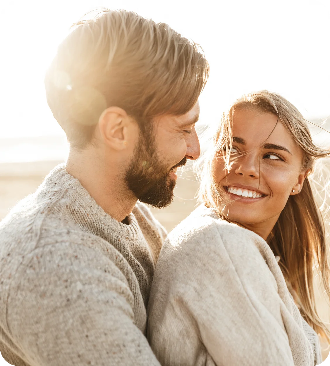 Happy couple smiling at each other in warm sunlight outdoors, wearing cozy sweaters in intimate moment - In Los Angeles, CA