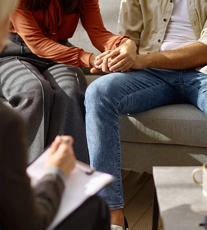 Couple holding hands during relationship counseling therapy session with therapist taking notes - Relational therapy in Los Angeles, CA